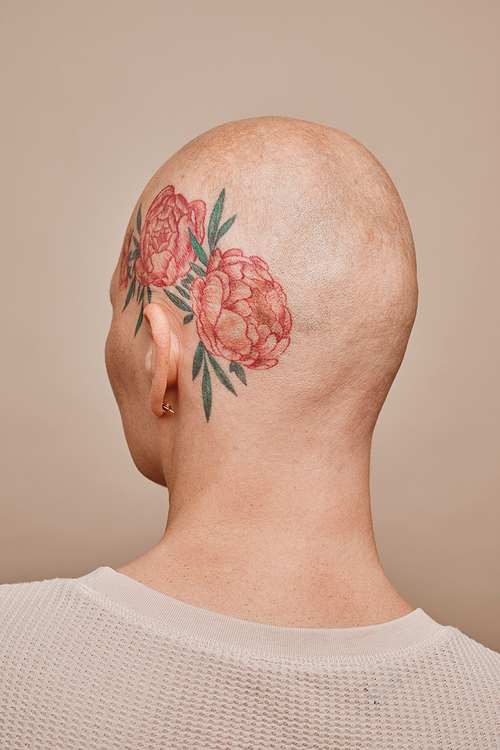 Minimal back view portrait of bald woman with head tattoo posing against beige background in studio, alopecia and cancer awareness