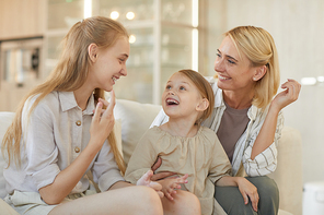Cute warm-toned portrait of carefree young mother talking to two daughters and smiling cheerfully while enjoying time together at home