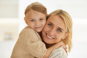 Warm-toned close up portrait of cute little girl embracing happy mother with love while looking at camera and smiling, copy space