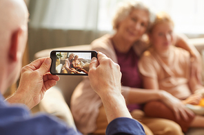 Portrait of senior man taking smartphone photo of wife and granddaughter for family memories, focus on smartphone screen, copy space