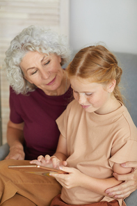Vertical high angle portrait of cute red haired girl teaching grandma how to use digital tablet