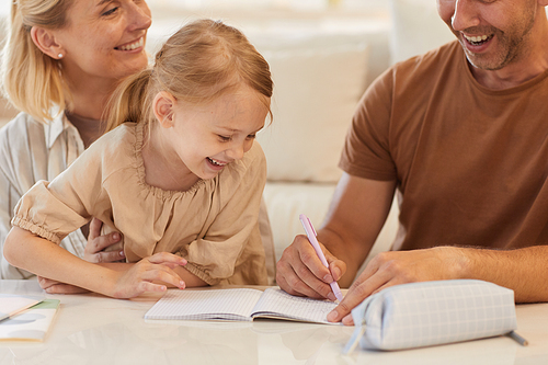 Close up portrait of cute little girl smiling happily with parents helping her draw or study at home, copy space