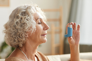 Side view close up portrait of senior woman using inhaler for asthma or breathing problems in home setting