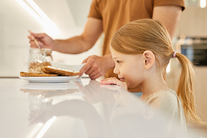 Side view portrait of cute little girl looking at tasty sandwiches while waiting for breakfast in kitchen, copy space
