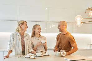 Warm-toned waist up portrait of modern happy family enjoying breakfast together while standing by table in minimal kitchen interior, copy space