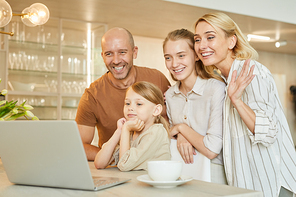 Warm-toned portrait of modern happy family waving at camera while speaking by video chat with relatives, copy space