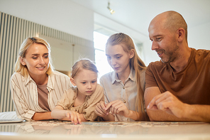 Warm-toned low angle portrait of modern family with two kids solving puzzle together while enjoying time indoors at home, copy space