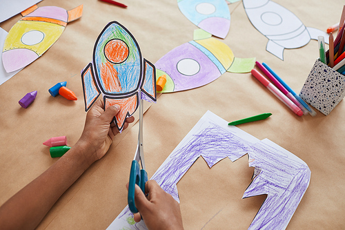 Close up of unrecognizable African-American boy cutting picture of space rocket while enjoying art and craft class in school or children development center, copy space