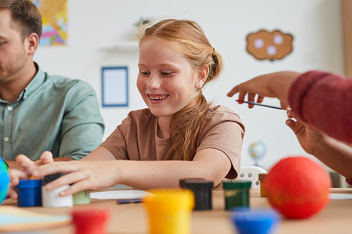 Portrait of cute red haired girl painting pictures while enjoying art and craft lesson in school or development center, copy space