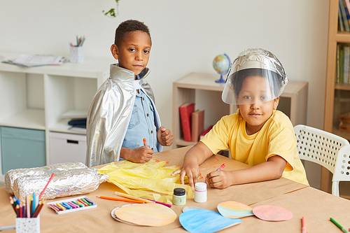 Portrait of two African-American boys playing astronauts and looking at camera while enjoying art and craft lesson in preschool or development center, copy space