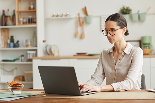 Portrait of elegant businesswoman wearing glasses while using laptop at cozy home office workplace, copy space