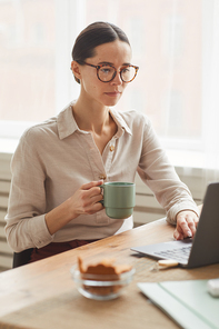 Vertical portrait of elegant businesswoman wearing glasses while using laptop at cozy home office workplace