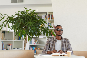 Front view portrait of blind African-American man reading Braille book in library, copy space