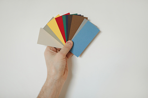 Close up of make hand holding color samples to white wall while choosing design for house redecorations, copy space