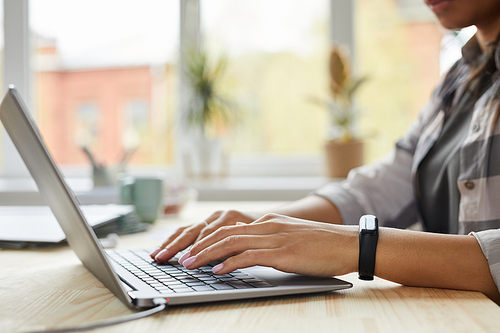 Side view close up of young mixed-race woman using laptop while working at home office, hands typing on keyboard, copy space