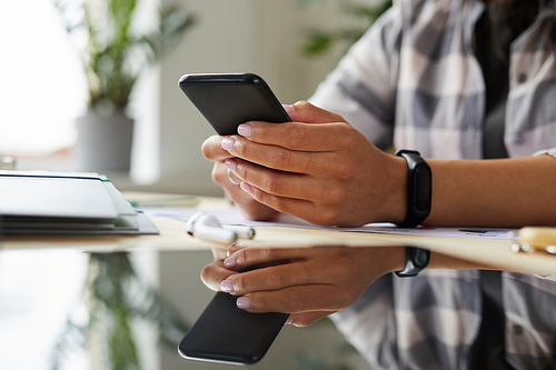 Close up of unrecognizable mixed-race woman using smartphone while working at home office, hands holding phone, copy space