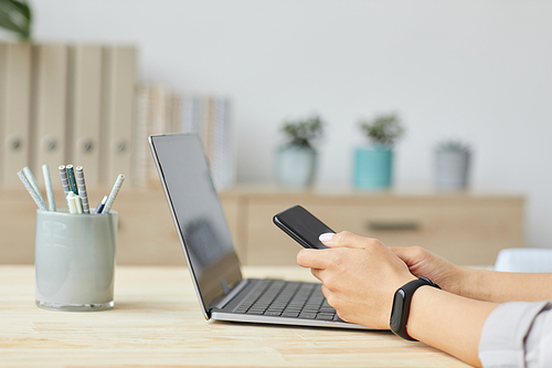 Side view close up of unrecognizable young woman holding smartphone over laptop while working at home office, copy space