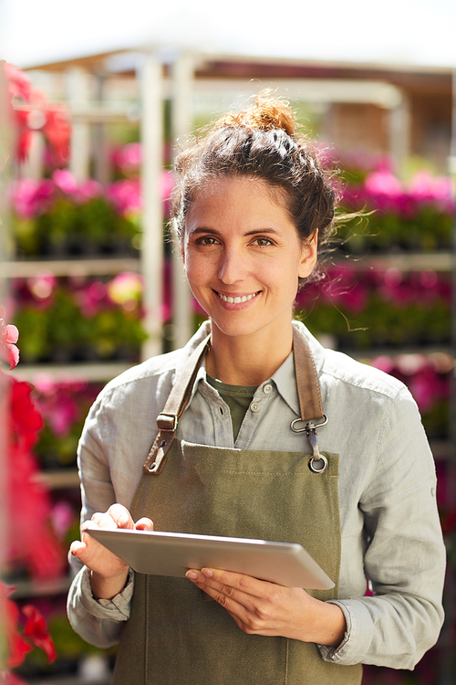 Vertical waist up portrait of smiling young woman holding digital tablet and looking at camera while enjoying work in plantation outdoors, copy space