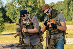 Young American men in vests and caps checking rifles before shooting at military base