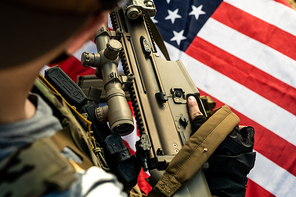 Close-up of American soldier holding own rifle above national flag while preparing for fight