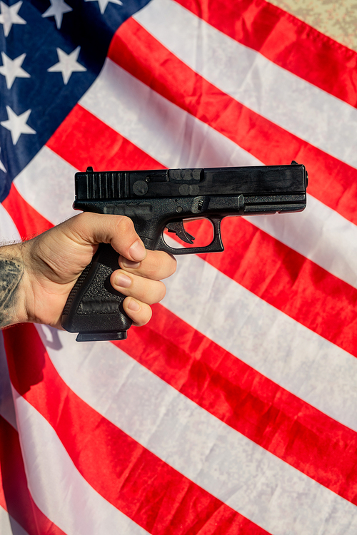Tattooed hand holding gun against American flag, carrying of weapons concept