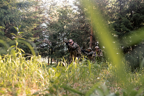 Group of armed soldiers with weapons patrolling forest in background, over grass view