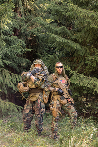 Portrait of serious young soldiers in camouflage outfits standing with weapon against forest trees