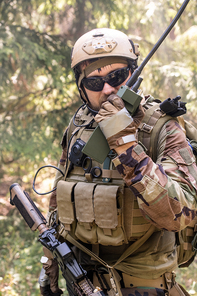 Portrait of soldiers in vest with necessary tools sending message through walkie-talkie in forest