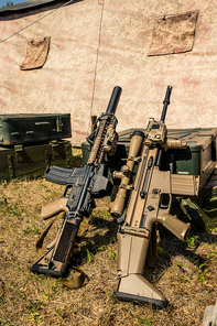 Two automatic rifles leaning on metal suitcase at military base, military camping