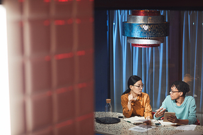 Wide angle portrait of two ethnic business people discussing project while working late in dark office, copy space