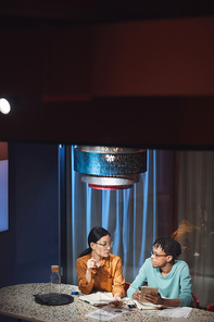 High angle portrait of two ethnic business people discussing project while working late in dark office, copy space