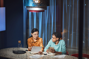 Portrait of two ethnic business people collaborating on project while working late in dark office, cop space
