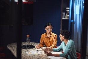 Portrait of Asian businesswoman talking to colleague while working late in dark office, cop space