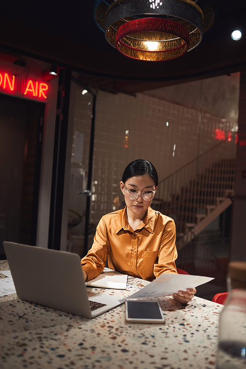 Vertical portrait of Asian businesswoman using laptop while working late in dark office, copy space