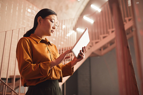 Side view portrait of young Asian businesswoman using tablet while standing by stairs outdoors, copy space