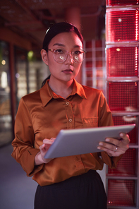 Waist up portrait of contemporary Asian businesswoman looking at camera while posing in futuristic office interior
