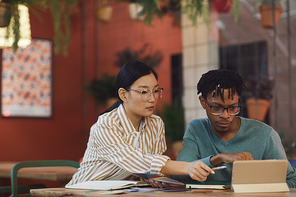 Portrait of two ethnic young people working on project together while sitting at table in cafe, copy space