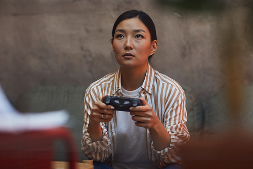Portrait of young Asian woman playing videogames via gaming console, copy space