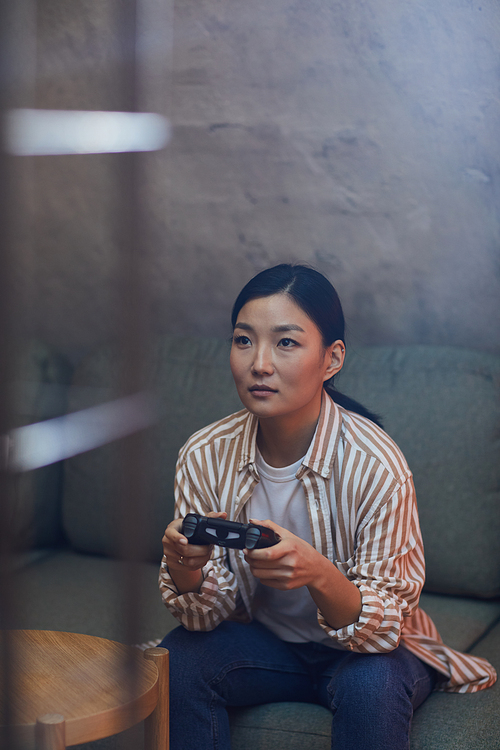 Vertical portrait of young Asian woman playing videogames via gaming console