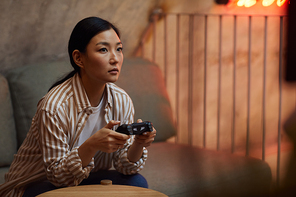 Portrait of young Asian woman holding gamepad controller while playing videogames via gaming console, copy space