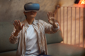 Waist up portrait of Asian woman wearing VR gear and gesturing while enjoying immersive experience in futuristic interior, copy space