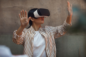 Waist up portrait of Asian woman wearing VR gear and gesturing while enjoying immersive experience in futuristic interior