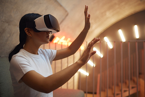 Side view portrait of Asian woman wearing VR gear and gesturing while enjoying immersive experience in futuristic interior, copy space