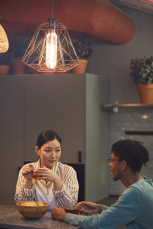Portrait of ethnic young couple enjoying drinks while chatting at table in cafe, copy space