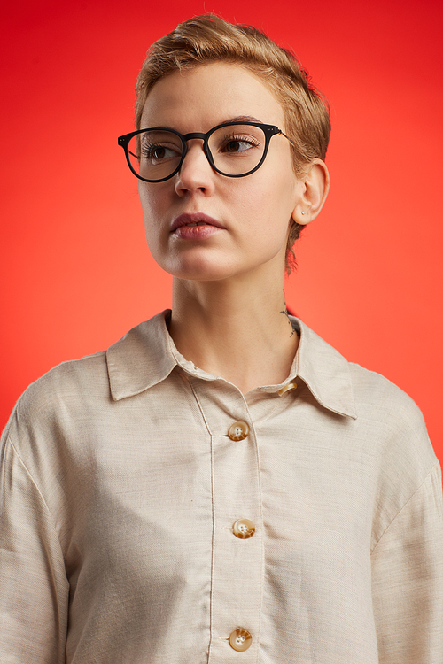 Portrait of modern woman wearing black rimmed glasses with short pixie haircut standing against fiery red background in studio