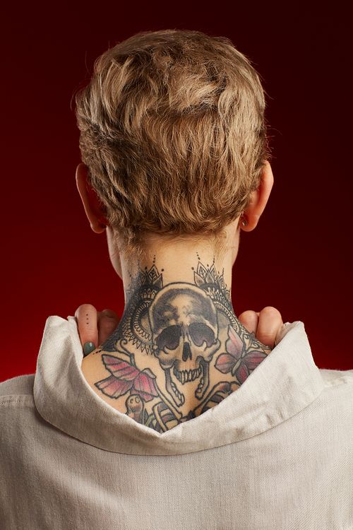 Back view of neck tattoo featuring scull and butterflies on short haired young woman posing against red background