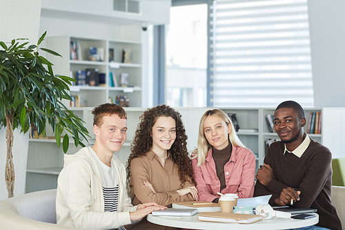 Multi-ethnic group of smiling young people looking at camera while studying together sitting at table in college library, copy space