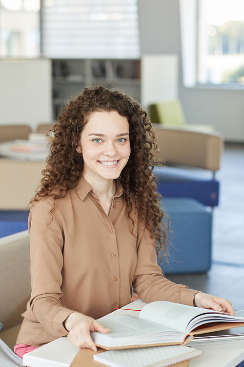 Vertical portrait of beautiful curly haired girl smiling at camera while studying in college library