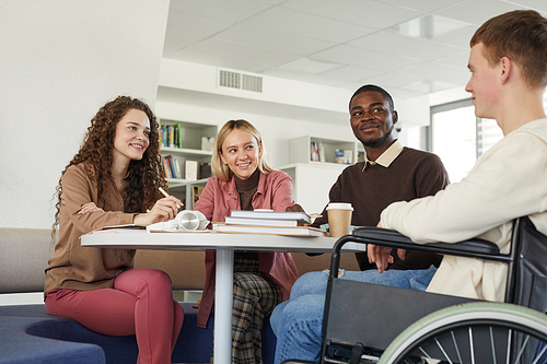 Low angle view at multi-ethnic group of students studying in college library featuring young man using wheelchair in foreground