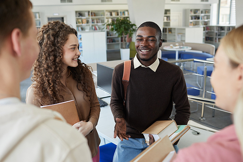 High angle portrait of multi-ethnic group of students chatting in college library with focus on smiling African-American man talking to friends